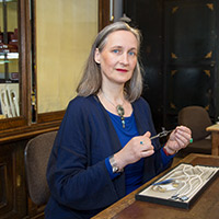 Blonde Frau mit dunkelblauer Jacke in einem Juweliergeschäft mit einer Perlekette beschäftigt